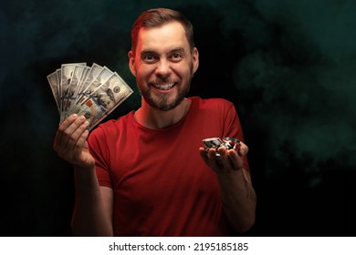 Studio Portrait Of Happy Smiling Young Man Posing With A Stack Of Poker Chips And Ward Of Dollar Banknotes In Hands Over Black Background With Smoke Effect. Gambling, Betting, Poker, Casino Concept.