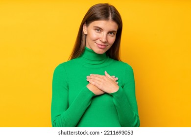 Studio Portrait Of Happy Thankful Woman Saying Thank You, Holding Hands On Heart Gratefully, Expressing Gratitude, Standing On Yellow Background In Green Turtleneck