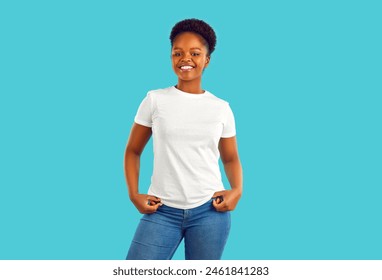 Studio portrait of happy woman in casual clothes. Beautiful confident young African American girl in blue jeans and white mockup T shirt standing isolated on turquoise background. Fashion concept - Powered by Shutterstock