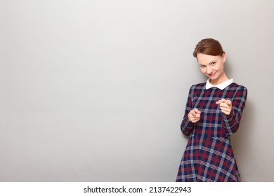 Studio Portrait Of Happy Young Woman Pointing With Fingers At You, Selecting You, Saying You Are Really Cool, Smiling Joyfully, Wearing Checkered Dress, Standing Over Gray Background, With Copy Space