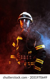 Studio Portrait Of Male Firefighter Dressed In Uniform And Oxygen Mask Covered In Smoke Over Black Background In Neon Lights. Concept Of Different Professions And Unusual People.