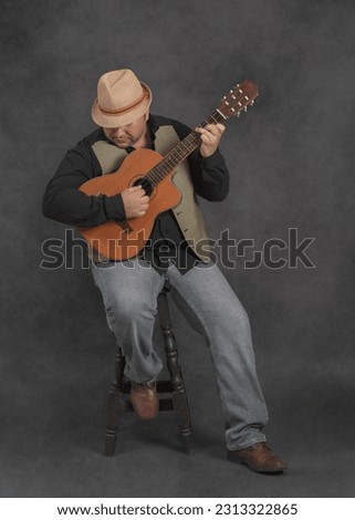 Studio portrait of man wearing a hat playing an old Cuban tres.
