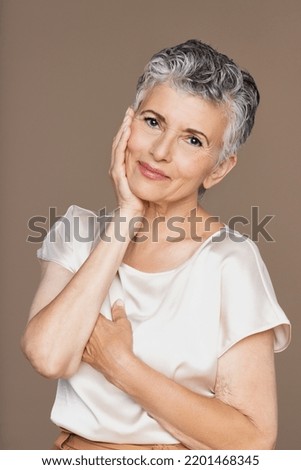 Studio portrait of a mature Latina woman in her 60's smiling on a neutral background.