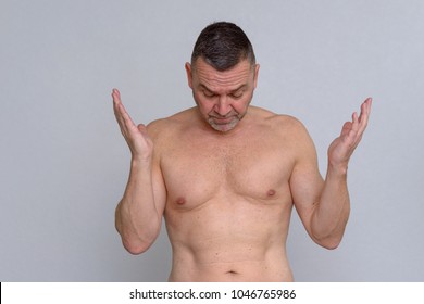 A Studio Portrait Of A Mature Man Naked From The Waist Up Looking Frustrated As He Throws His Hand In The Air.
