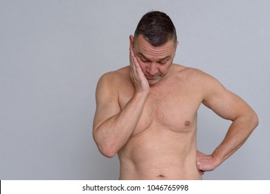 A Studio Portrait Of A Mature Man Naked From The Waist Up Looking Fed Up And Depressed.