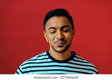 Studio portrait of mid adult non-binary with eyes closed against red background