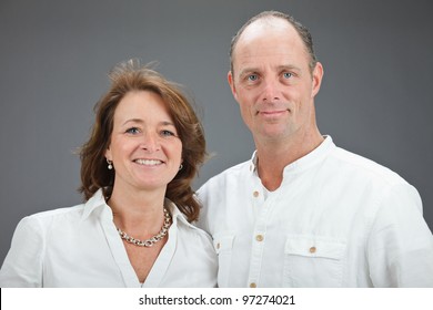 Studio Portrait Of Middle Aged Couple Wearing White Shirt Isolated On Grey Background