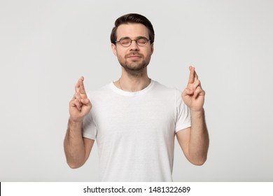 Studio portrait millennial guy in eyeglasses crossing fingers, hope for good luck, isolated on grey white background. Superstitious young man waiting for test results, good outcome or miracle.