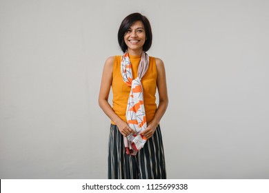 Studio Portrait Of An Older And Attractive Chinese Asian Woman Against A White Backdrop. She Is Smiling And Is Wearing An Orange Sweater, A Dark Dress And Has A Scarf Draped Over Her Neck. 