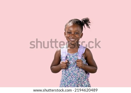 studio portrait with pink background of a happy little girl wearing backpack for school
