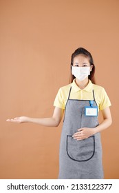 Studio Portrait Of Positive Young Coffeeshop Barista In Medical Mask Protecting Against Coronavirus Inviting Customers
