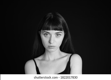 Studio portrait of a pretty brunette woman in a black spaghetti strap top, looking at the camera, against a plain black background - Powered by Shutterstock