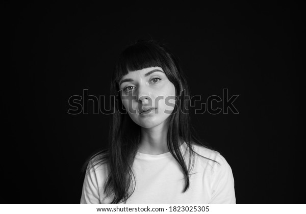 Studio portrait of a pretty brunette woman in a\
white blank t-shirt, against a plain black background, looking at\
camera