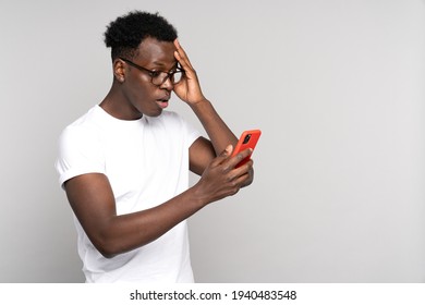 Studio portrait of puzzled African American man scratching head, holding and looking at screen cellphone, thinking, plans or reconsiders something isolated on grey background. Shocked message. 