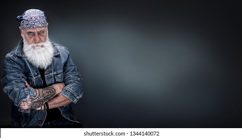 studio portrait of a senior hipster with tattooed arms, wearing a bandana and a long white beard. panoramic head