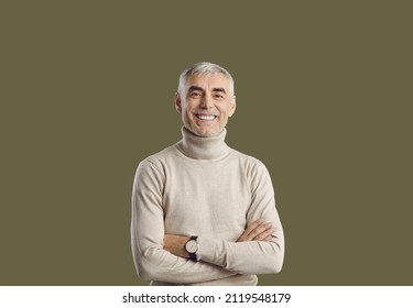 Studio portrait of senior man with happy face expression. Cheerful, smiling man wearing turtleneck sweater and wristwatch looking at camera standing with arms folded isolated on solid green background - Shutterstock ID 2119548179