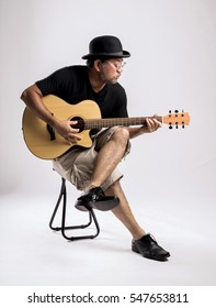 Studio Portrait Of Senior Man With Hat Playing Guitar.