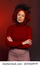 Studio Portrait Of A Serious Woman 35-40 Years Old With Red Hair And A Crown On Her Head In The Form Of Snakes On A Colored Background.