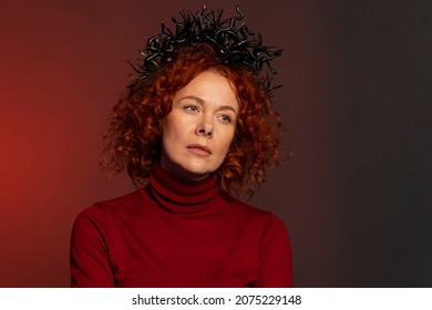 Studio Portrait Of A Serious Woman 35-40 Years Old With Red Hair And A Crown On Her Head In The Form Of Snakes On A Colored Background.