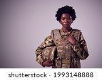 Studio Portrait Of Serious Young Female Soldier In Military Uniform Against Plain Background