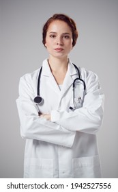 Studio Portrait Of Serious Young Female Doctor Wearing White Coat Against Plain Background