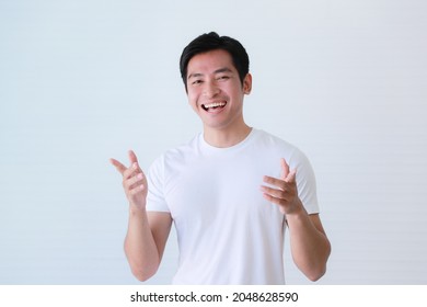 Studio Portrait Shot Of Asian Happy Young Handsome Smart Teenager Teen Guy Male Model In Casual T Shirt Clothing Smiling Laughing Show Teeth Look At Camera Raising Hands Up On White Background.