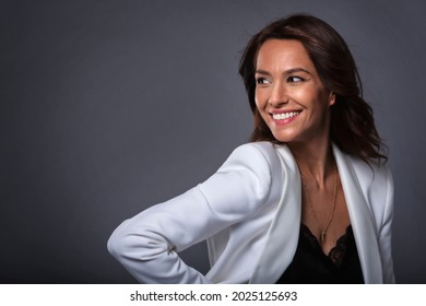 Studioporträt einer attraktiven Frau mittleren Alters mit zahnfreundlichem Lächeln, die einen Blazer trägt, während sie auf dunkelgrauem Hintergrund steht. Kopiert Platz. 