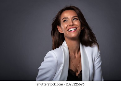 Studio Portrait Shot Of Attractive Middle Aged Woman With Toothy Smile Wearing Blazer While Standing At Isolated Dark Grey Background. Copy Space. 