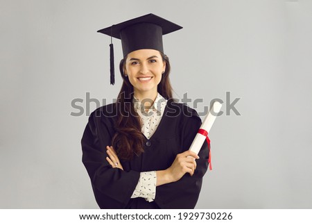 Studio portrait of smart student with graduation certificate. Happy graduate of prestigious academy, college or university standing against gray background, holding her diploma and smiling at camera