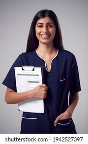 Studio Portrait Of Smiling Female Nurse With Clipboard Wearing Uniform Against Plain Background