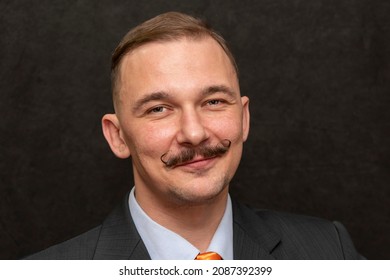 Studio Portrait Of A Smiling Man 30-35 Years Old, Dark-haired With A Thin Mustache, In A Suit And Tie On A Black Background.