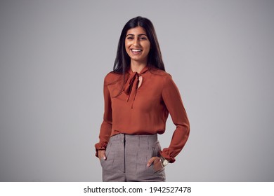 Studio Portrait Of Smiling Young Businesswoman With Hands In Pockets Against Plain Background