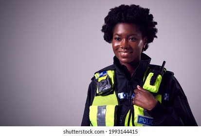 Studio Portrait Of Smiling Young Female Police Officer Against Plain Background