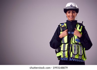 Studio Portrait Of Smiling Young Female Police Officer Against Plain Background