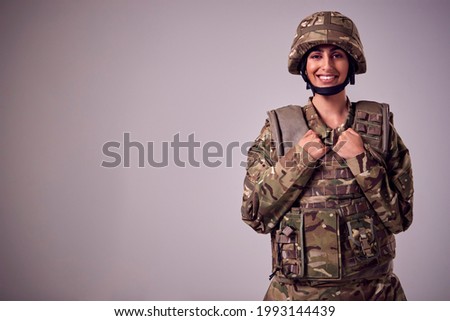 Studio Portrait Of Smiling Young Female Soldier In Military Uniform Against Plain Background