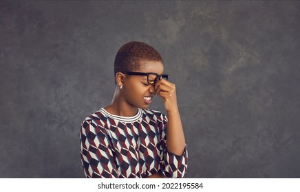 Studio portrait of stressed black lady cringing at mistake or rubbing dry tired eyes and nose bridge. Oh no not again. It's fiasco. I forgot these dumb idiotic hopeless morons make me feel embarrassed