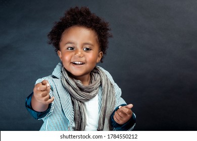 Studio Portrait Of A Stylish Little African Boy With Curly Hair Isolated On Dark Background. Kids Fashion. Kids Clothes.