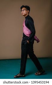 Studio Portrait Of A Tall And Handsome Malay Asian Man In A Traditional Black Baju Melayu Outfit With A Festive Pink Sash Over His Shoulder. He Is Dressed To Go Visiting During Ramadan. 