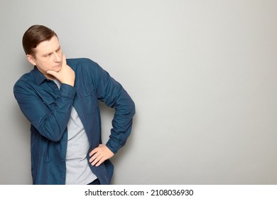 Studio portrait of thoughtful mature man touching chin with hand, being deep in thoughts, trying to solve issue, making choice, planning, wearing shirt, standing over gray background, with copy space