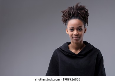 Studio portrait of a trendy attractive young Black woman in hoodie standing looking quietly at the camera with a smile on a grey background with copyspace - Shutterstock ID 1989926855