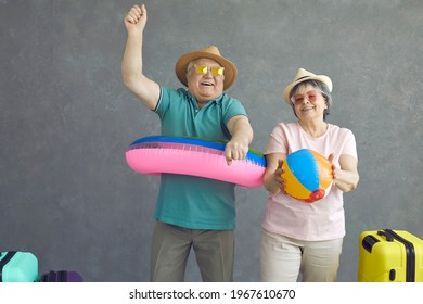 Studio portrait of two active elder tourists ready for tropical getaway travel summer vacation. Happy old people dancing and having fun with beach toys. Excited senior couple enjoying holiday shopping - Powered by Shutterstock