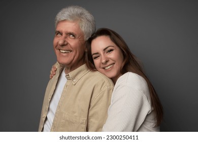 Studio portrait of a Ukrianian father in his 60s and his adult daughter in her late 20s. They are both wearing light colours and the daughter is hugging her father. The background is grey. - Powered by Shutterstock