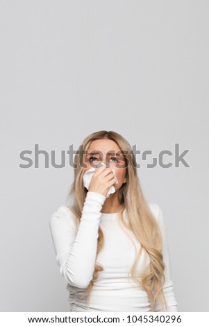 Studio portrait of unhealthy cute blonde female in white top with napkin blowing nose, looks up to the source of the allergy, source of unpleasant odor/Place for advertising/Rhinitis, allergy concept Stock photo © 