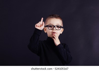 Studio Portrait Of Watchful Child In Black Pullover And Black Glasses On Black Background