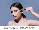 Studio portrait of a woman applying cosmetic tonal foundation on face using makeup brush. Beautiful girl doing contouring apply blush on cheeks isolated on studio background.