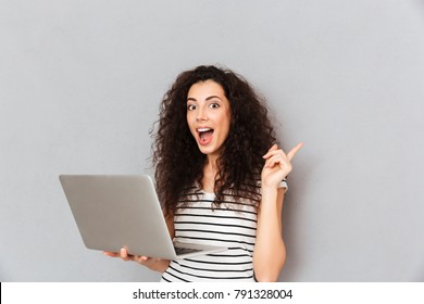 Studio portrait of woman with curly hair being excited to find useful information in internet via silver computer, gesturing eureka with index finger - Shutterstock ID 791328004