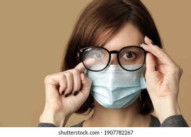 Studio portrait of woman with foggy glasses caused by wearing disposable mask. Protective measure during coronavirus pandemic. Medical mask and glasses fogging concept.