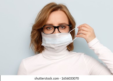 Studio Portrait Of Woman In Glasses Wearing Face Medical Mask, Looking At Camera, Isolated On Blue Background. Flu Epidemic, Dust Allergy, Protection Against Virus. Covid-19, Coronavirus Pandemic