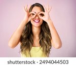 Studio, portrait and woman with okay on eyes for comedy, humor and funny gesture on pink background. Female person, smile and happy with emoji sign for comic satisfaction, confidence and silly face