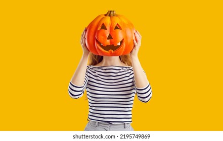 Studio portrait of a woman with a pumpkin head. Funny young girl standing isolated on a yellow background, holding a carved orange pumpkin and hiding her face behind it. Halloween concept - Shutterstock ID 2195749869